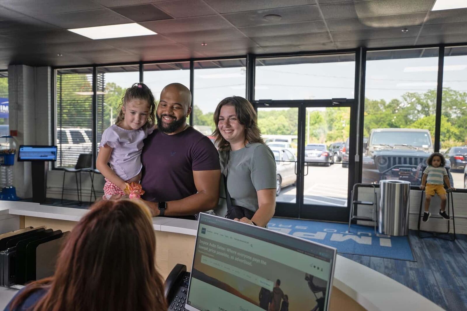 A family with their sales associate at the front desk of the Impex Auto Sales showroom in Greensboro